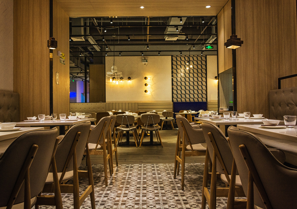 Iluminação comercial para restaurantes modernos com luminárias pendentes e luz quente destacando mesas e cadeiras claras.